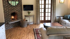 A cozy living room with a brick fireplace, a flat-screen TV, a comfortable sofa, and a large window with curtains.