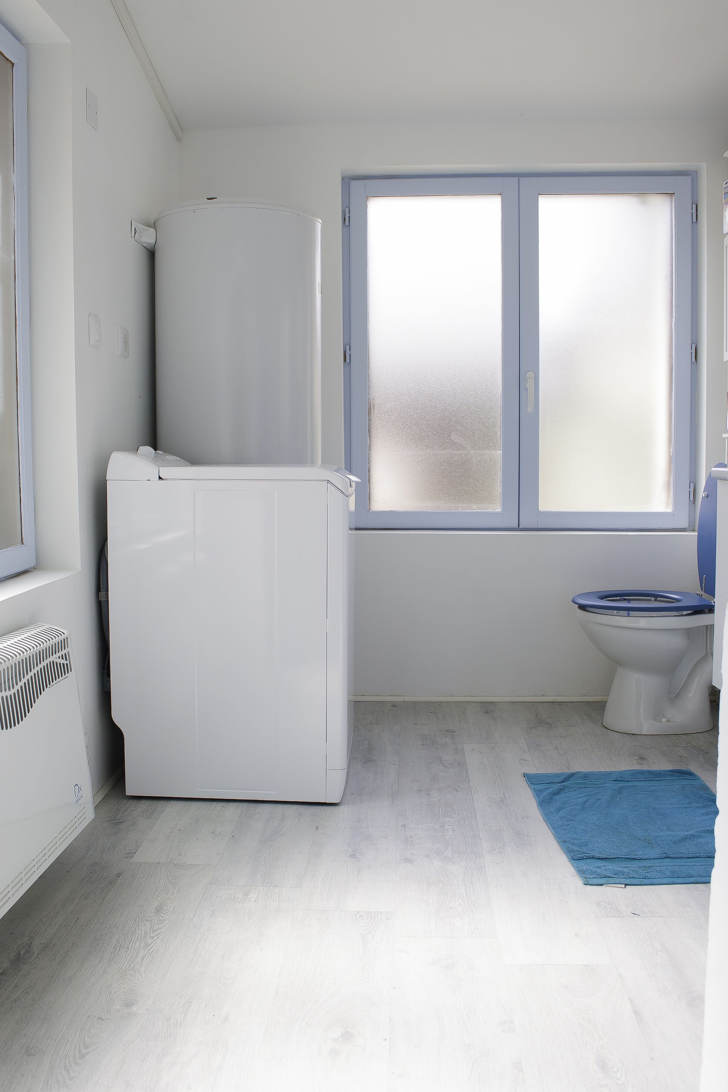 Une salle de bain avec un radiateur blanc, un lave-linge blanc, des toilettes et une fenêtre à vitre dépolie.