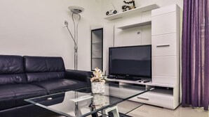 Un salon moderne avec un canapé en cuir noir, une table basse en verre, un téléviseur à écran plat et un meuble de rangement blanc.