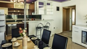 Un espace repas moderne avec une longue table dressée pour quatre personnes, entourée de chaises noires. Un vase contenant des fleurs blanches est posé sur la table.