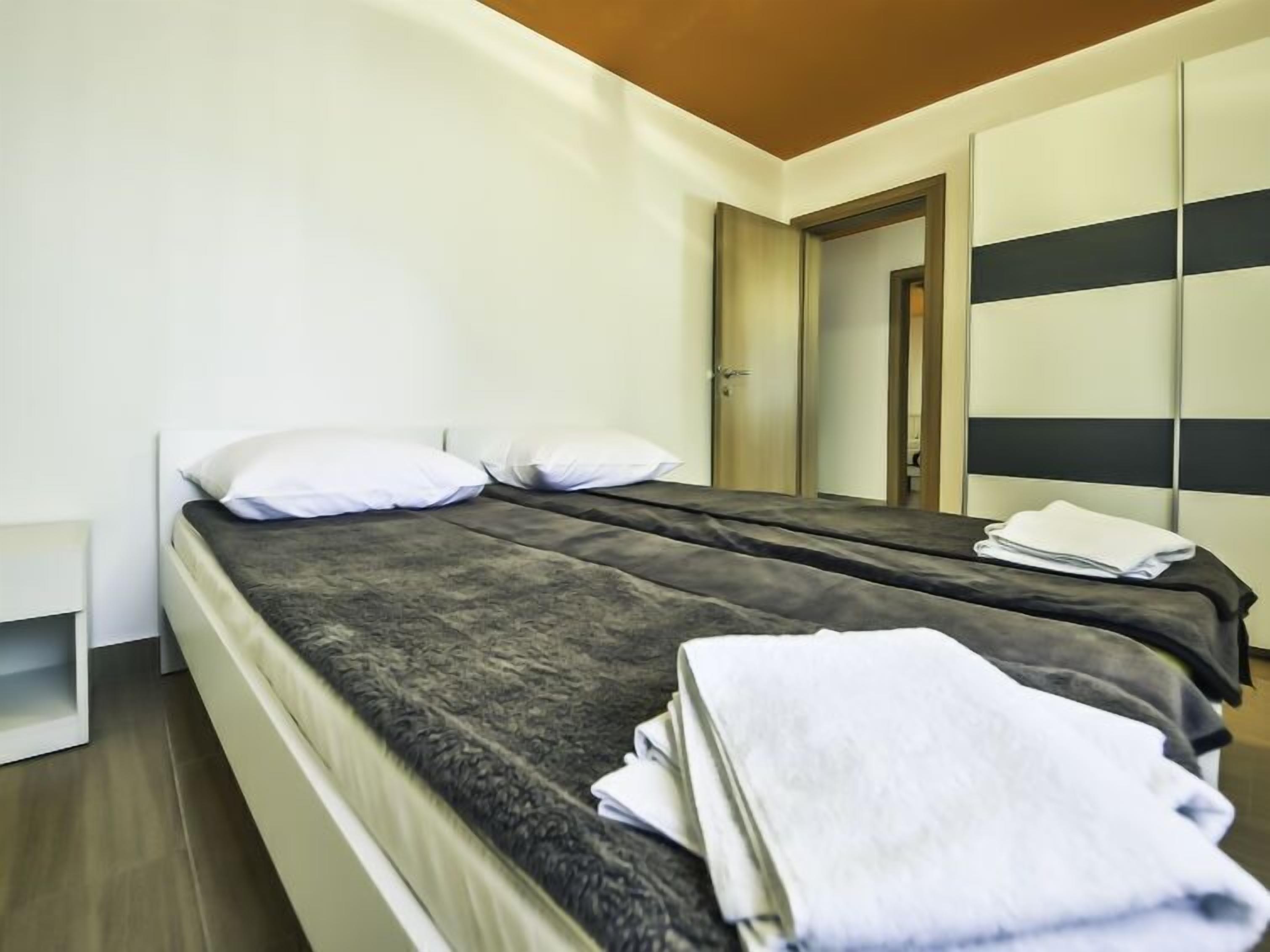 A modern hotel room with a bed, a wardrobe, and a door leading to another room.