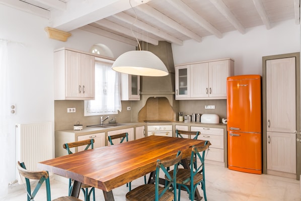 A kitchen with a wooden table, teal chairs, white cabinets, and an orange refrigerator.