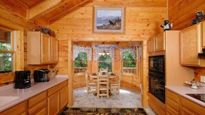A wooden cabin interior with a dining table, chairs, kitchen area, and a view of the outdoors.