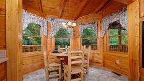 A wooden cabin interior with a round dining table, chairs, and a chandelier.