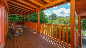 A wooden deck with a bench and railing, overlooking a lush green landscape.