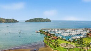 Un puerto deportivo con numerosas embarcaciones amarradas, rodeado de exuberante vegetación y un cielo azul despejado.