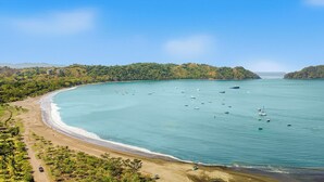 Paisaje costero con playa arenosa, mar tranquilo y barcos.