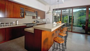 Una cocina moderna con armarios de madera, una isla grande con taburetes de bar y vistas al exterior a través de puertas correderas de cristal.