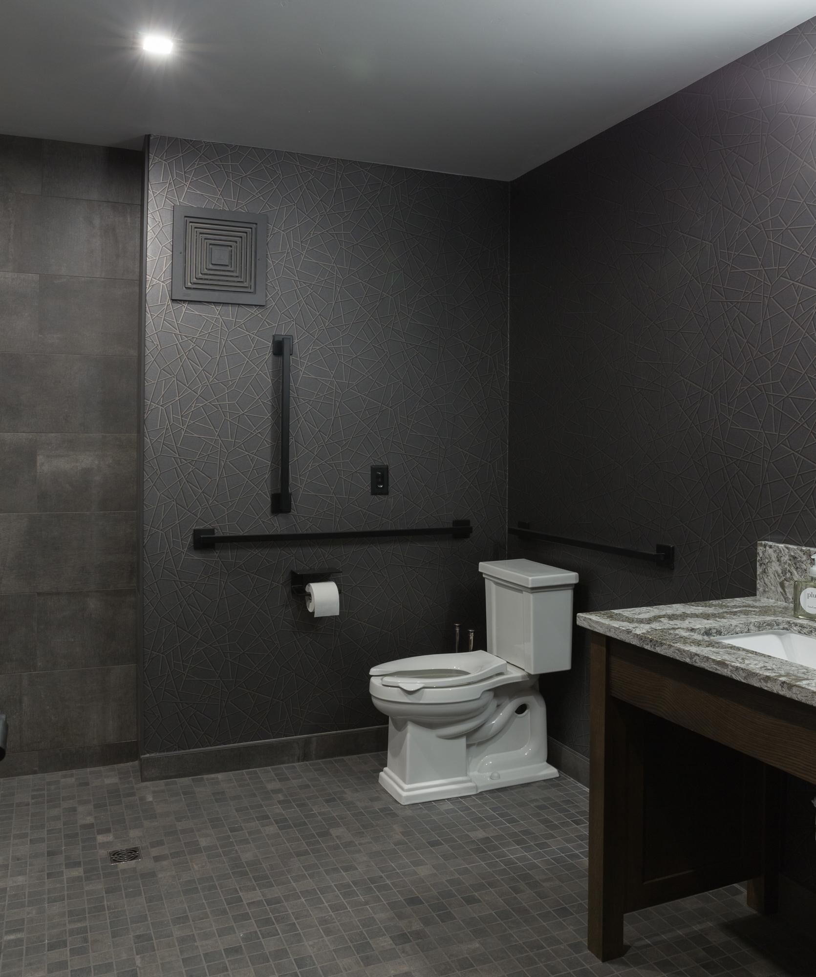 Une salle de bain moderne avec un mur texturé de couleur sombre, des toilettes blanches, un lavabo en marbre et un porte-serviettes.