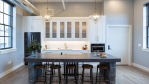A modern kitchen with white cabinets, a large island with stools, stainless steel appliances, and pendant lighting.