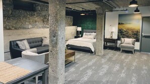 A modern room with exposed concrete pillars, a bed, a sofa, and a desk.