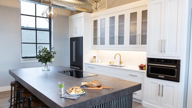 A modern kitchen with a large island, white cabinetry, and stainless steel appliances.