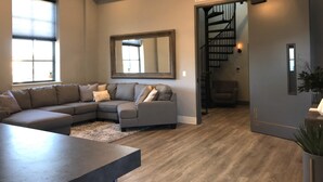 A modern living room with a sectional sofa, a dining table, and a staircase leading to another level.