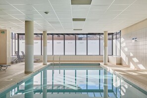 Una piscina con paredes de vidrio transparente, piso de baldosas e iluminación empotrada en el techo.