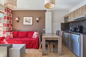 Un espacio habitable compacto con un sofá rojo, una mesa de comedor de madera y una kitchenette con electrodomésticos modernos.