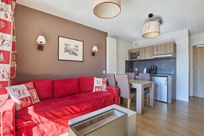 Una sala de estar moderna con un sofá rojo, una mesa de comedor y una zona de cocina con armarios de madera y un refrigerador.