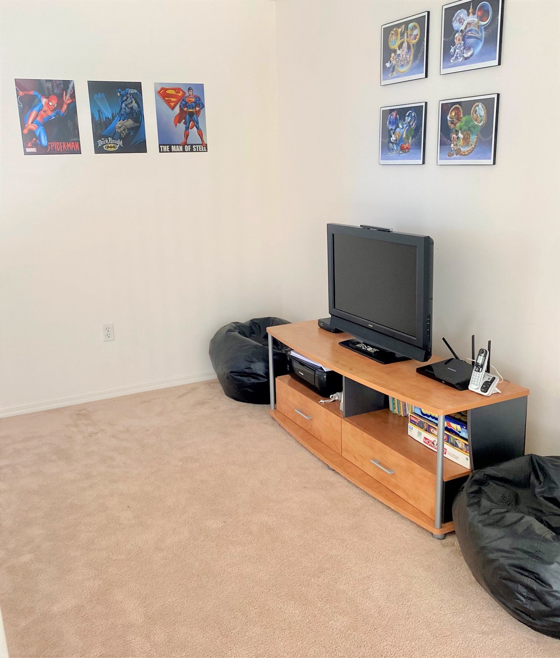 A room with a TV on a wooden stand, a carpeted floor, and four posters on the wall.