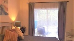 Une chambre avec un grand lit, un ventilateur de plafond, une fenêtre avec des rideaux et une vue sur l’extérieur.