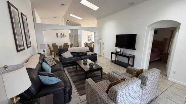 A living room with a sofa, armchair, coffee table, TV, and dining area. - Daisy's Den - Five Bedroom Home (Kissimmee)