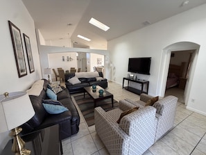 Sala de estar com sofá, poltrona, mesa de centro, televisão e área de jantar.
