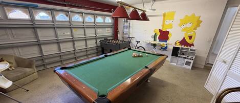 A pool table in a room with a garage door, a bicycle, and a wall mural of cartoon characters.
