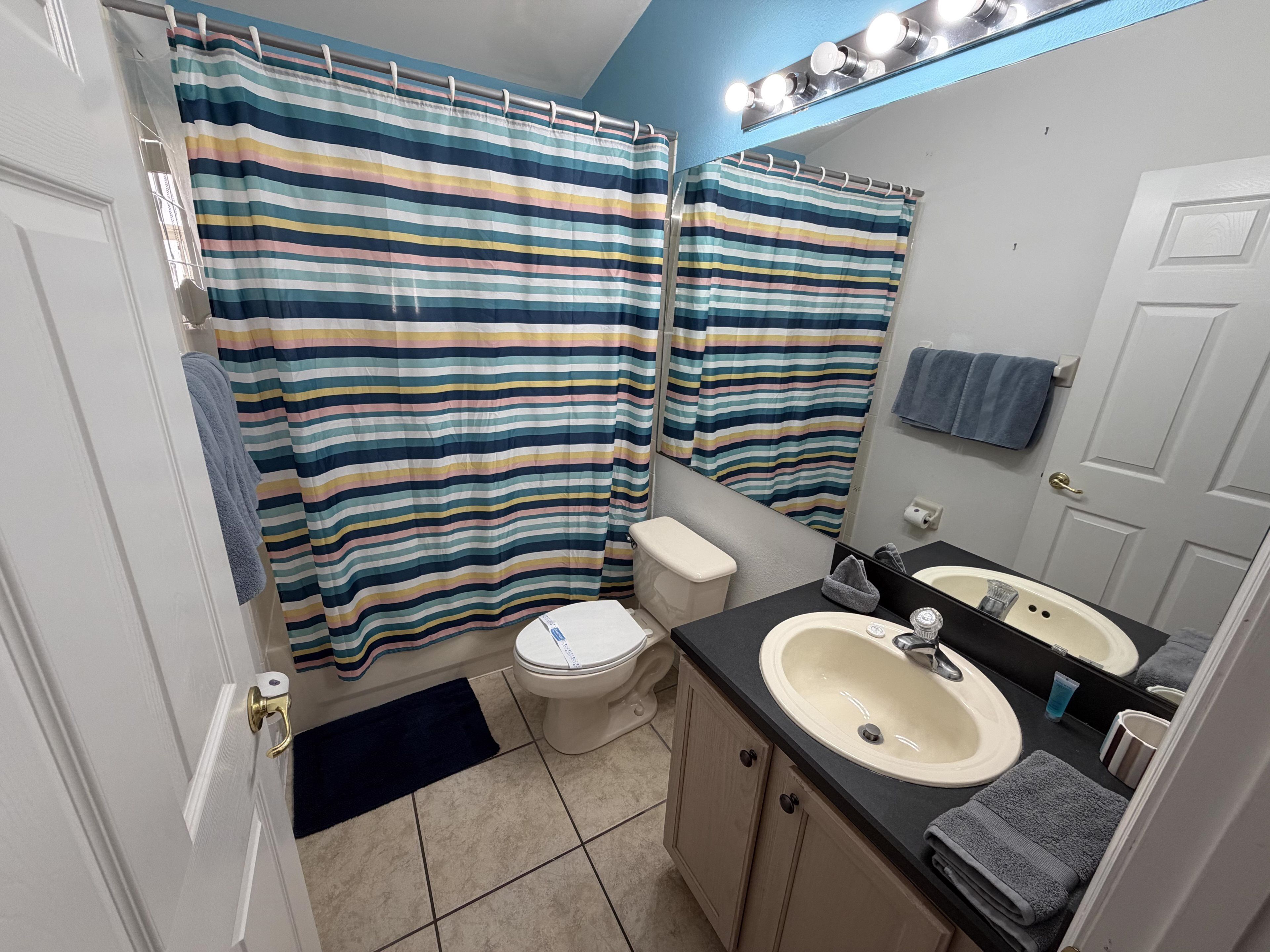 Un baño con inodoro, dos lavamanos, un espejo y cortinas de ducha a rayas.