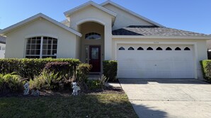 A single-story house with a garage, a front door, and a small garden with a statue. - Daisy's Den - Five Bedroom Home (Kissimmee)