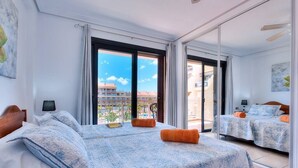 Habitación de hotel con dos camas, un amplio ventanal corredero al balcón y vista a la ciudad.