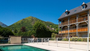 Hotel med pool, træbalkoner og et bjerglandskab i baggrunden.