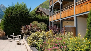 Et hotel med en træbalkon, en have med farverige blomster og et bjerg i baggrunden.