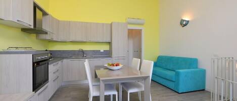 Una cocina compacta con electrodomésticos modernos, una mesa de comedor con sillas y una pared de color amarillo brillante.