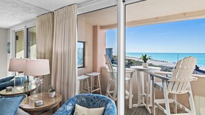 A balcony with a view of the beach, a table with chairs, and a sofa with a cushion labeled 'Beach House'. - Gulf view unit at Jetty East! One free beach set up daily. (Destin)