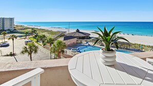 A balcony with a view of a beach, a pool, and a building in the background. - Gulf view unit at Jetty East! One free beach set up daily. (Destin)