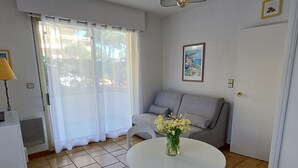A living room with a grey sofa, a white table with a vase of flowers, and a window with sheer curtains. - Antares by Interhome (Cavalaire)