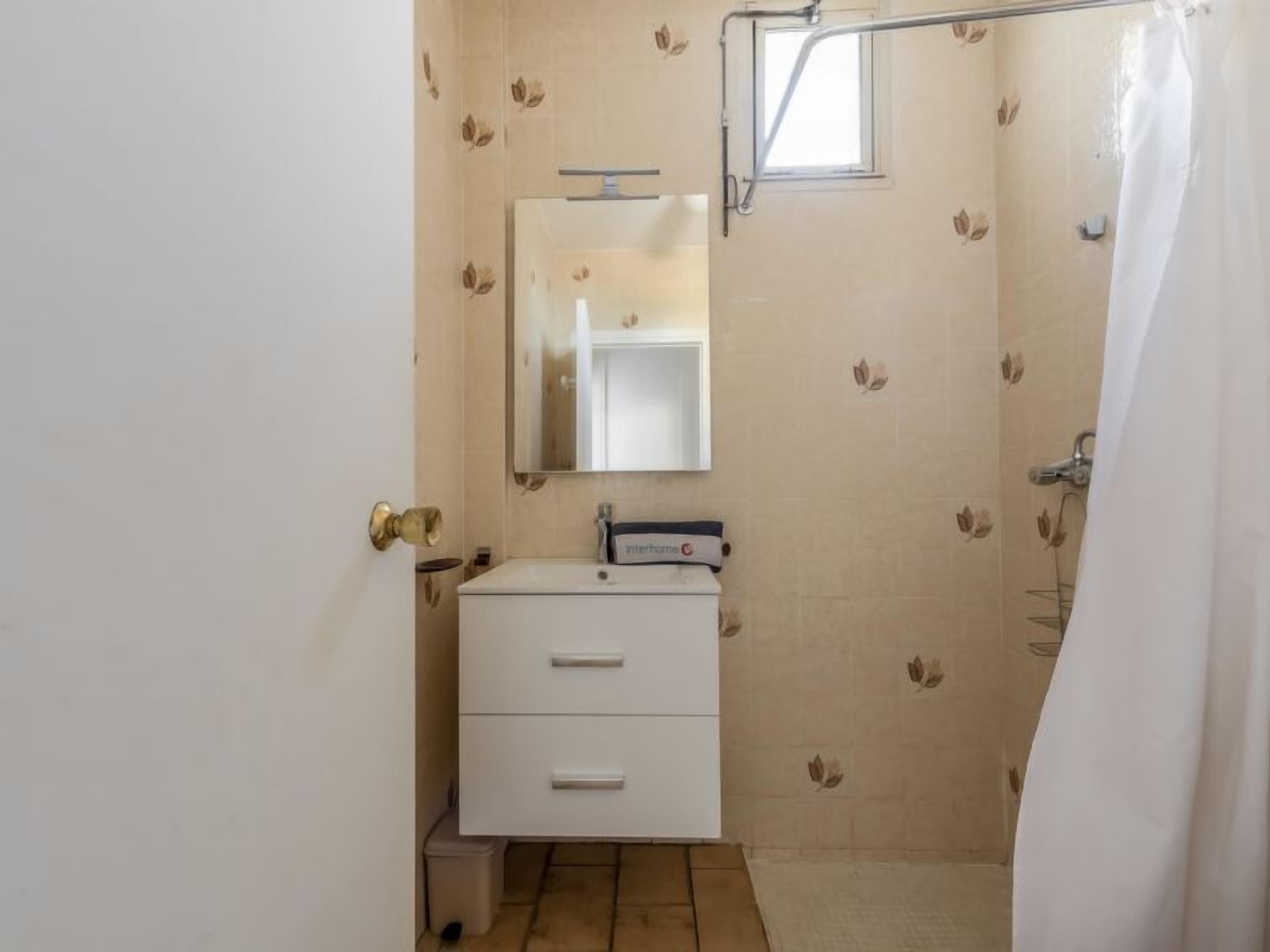 A small bathroom with a white sink, a mirror, and a shower curtain.