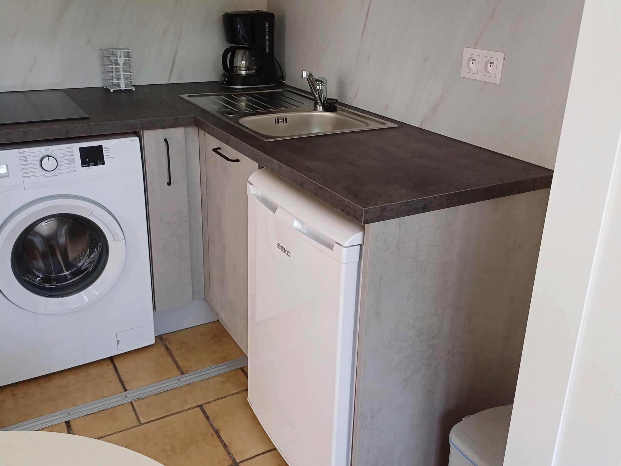 Une cuisine compacte équipée d’un lave-linge, d’une machine à café et d’un lave-vaisselle.