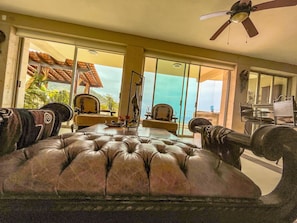 Relax in the spacious living area with a large sofa, ceiling fan, and sliding glass doors leading to a balcony with an outdoor view.