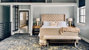 A spacious bedroom with a large bed, two bedside tables, a bench, a window, and a view of a hallway. - South Flat Luxury Suite - Full Kitchen, Adjustable King Bed, Full Bed in Loft (Logan)
