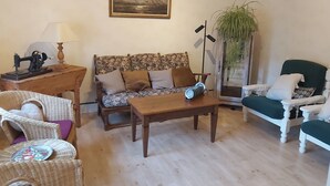 Un soggiorno accogliente con un divano, poltrone, un tavolino in legno, una lampada, una macchina da cucire e un quadro appeso al muro.
