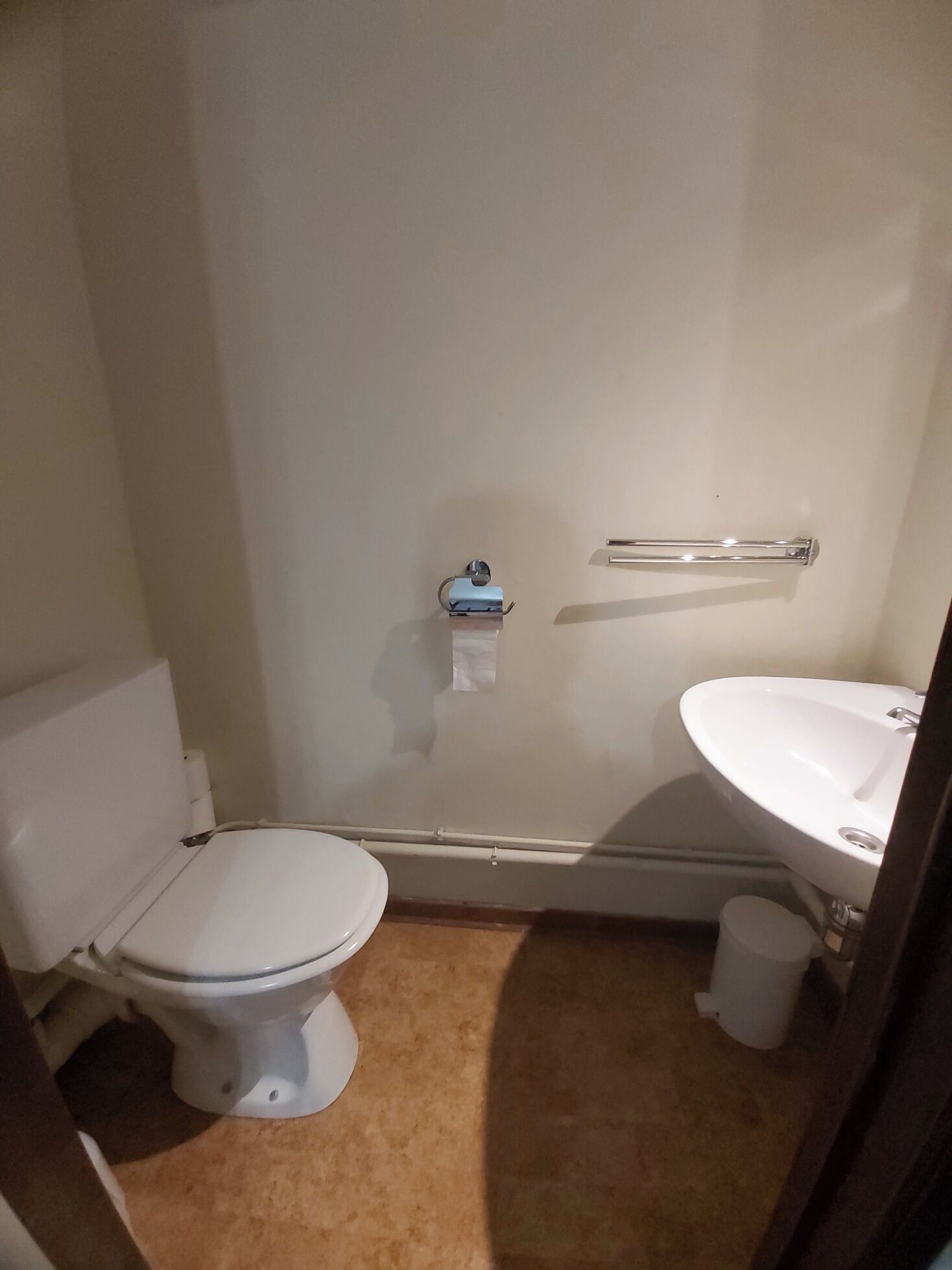 A small, compact bathroom with a toilet, sink, and a towel rack.