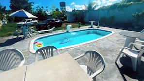 A rectangular swimming pool with a blue interior, surrounded by outdoor seating including plastic chairs and a table.