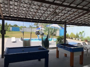 An outdoor pool area with a foosball table, a pool table, and a swing chair.
