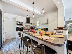 A modern kitchen with a central island, bar stools, pendant lighting, and a view of the living area.