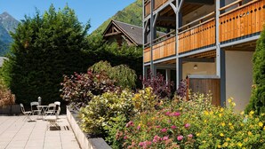 A hotel with a wooden balcony, a garden with colorful flowers, and a mountain backdrop.