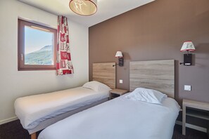 Ein Hotelzimmer mit zwei Einzelbetten, einem Fenster mit Bergblick und zwei Wandlampen.