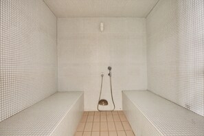 A small, tiled shower room with benches and a handheld showerhead.