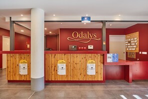 A reception desk with a red wall and the name 'Odaly's' in gold lettering. There are three wooden panels with signs indicating different locations.