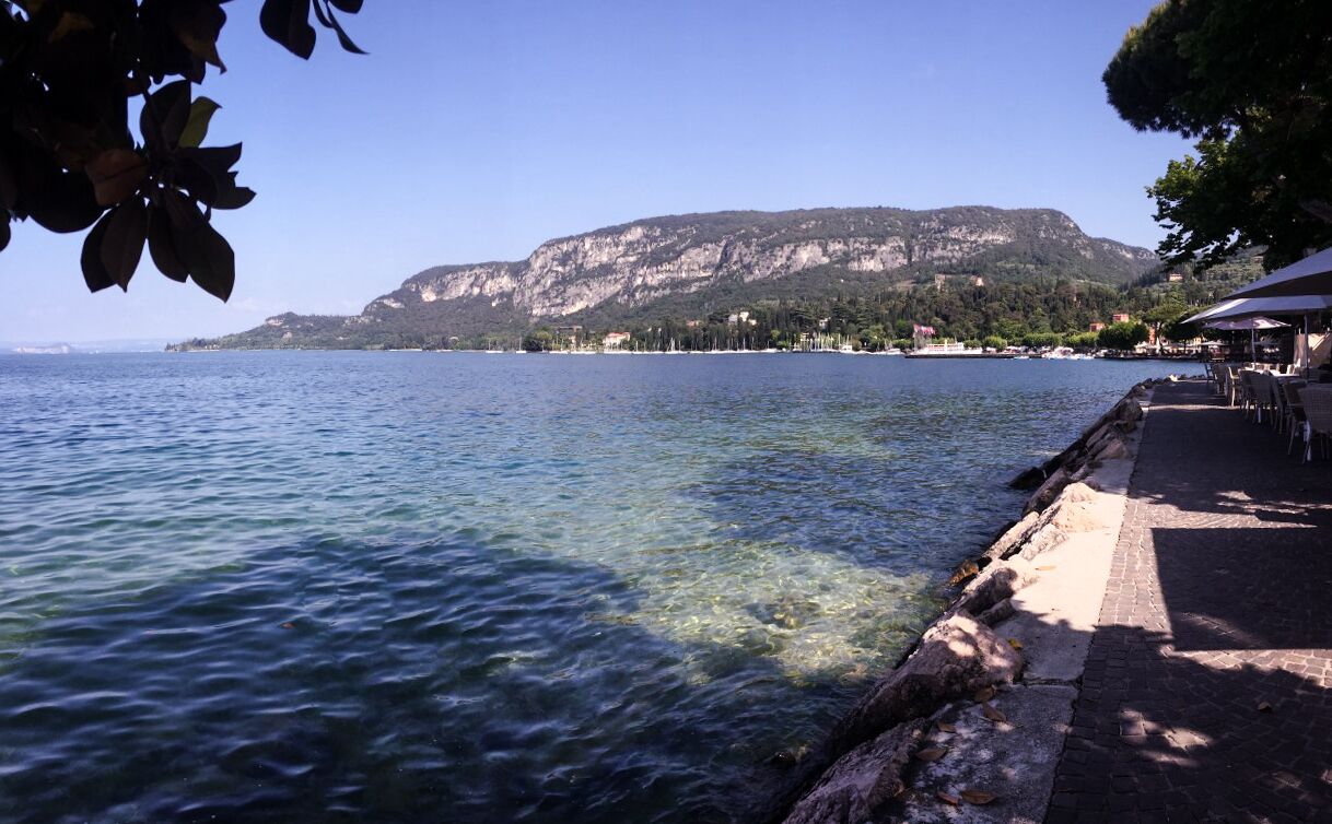 A waterfront view with a clear path leading to a seating area, overlooking a calm lake and a mountainous backdrop.
