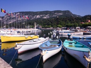 A marina with several small boats docked, a rocky mountain in the background, and flags flying.
