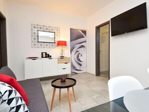 Una habitación de hotel moderna con un armario blanco, una mesita redonda con una vela, una lámpara roja y un cuadro abstracto grande en la pared.